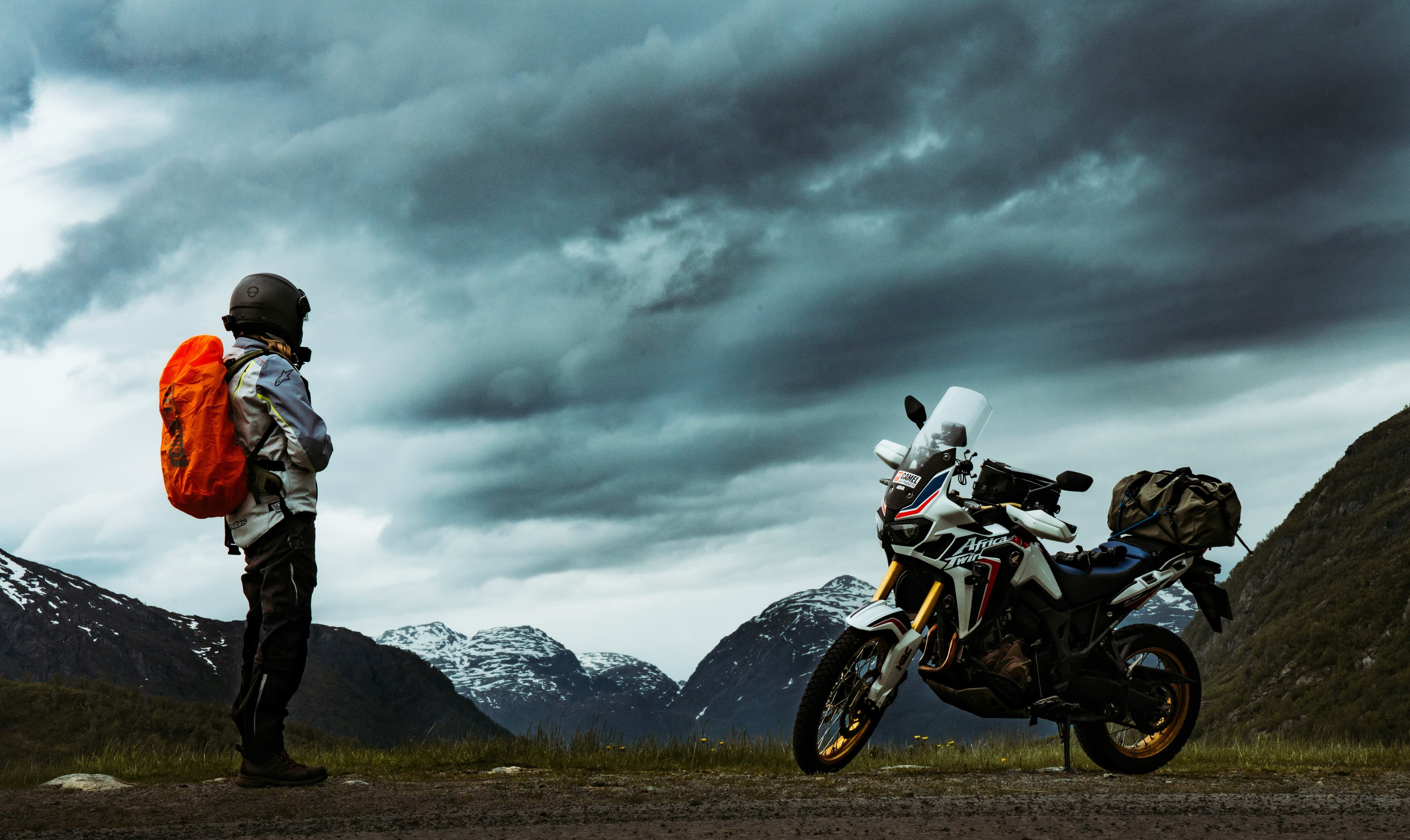 A rider beside a loaded adventure bike under a dramatic mountain sky
