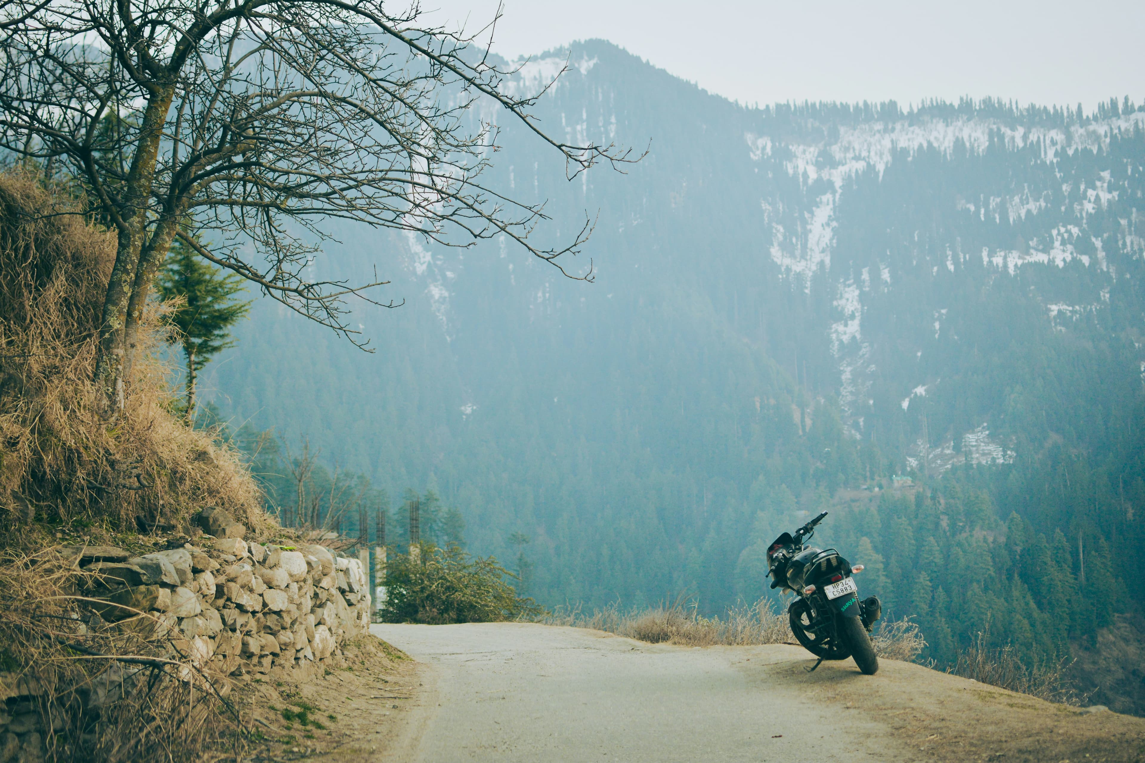 A motorbike parked on a gravel mountain road with mist hanging over forested peaks