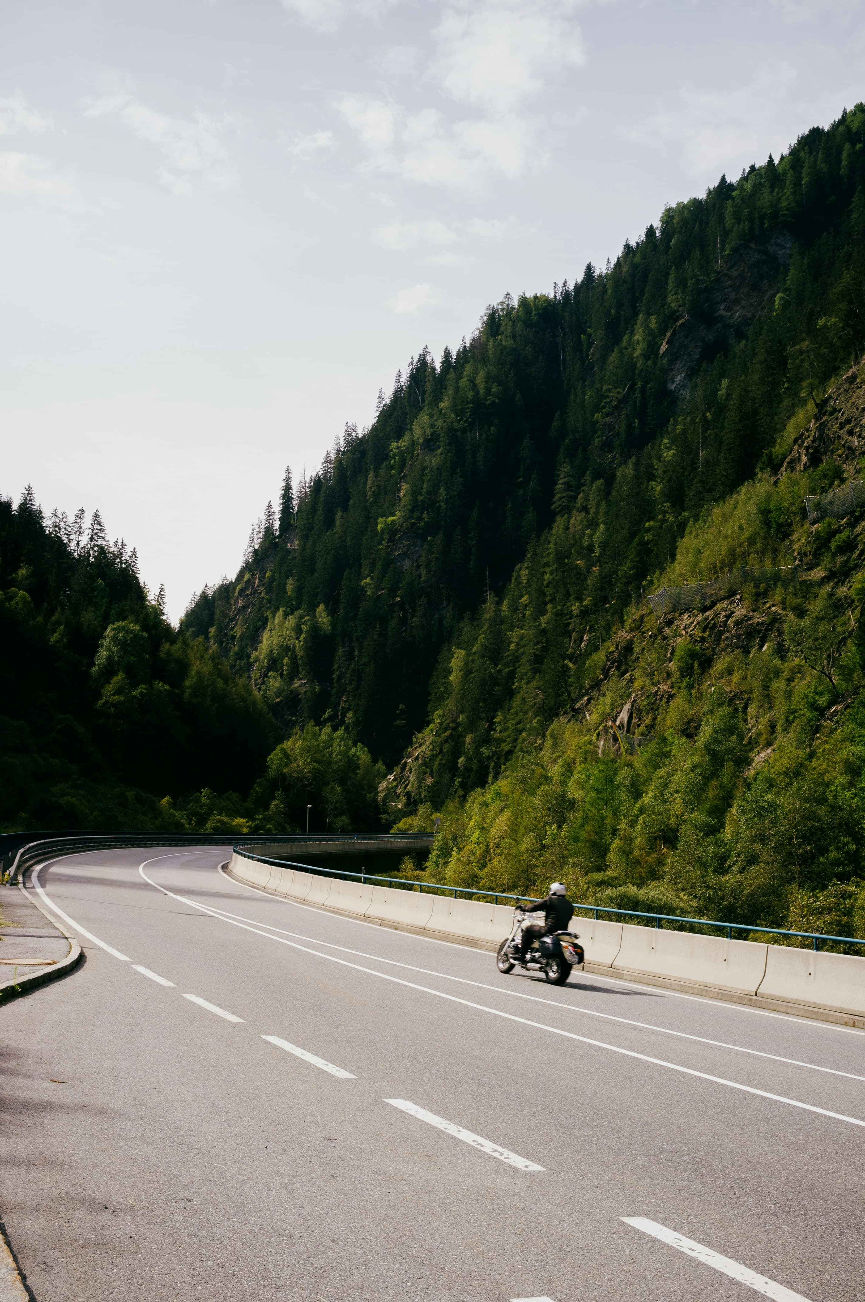 Rider on a wide curve beside a steep forested mountain