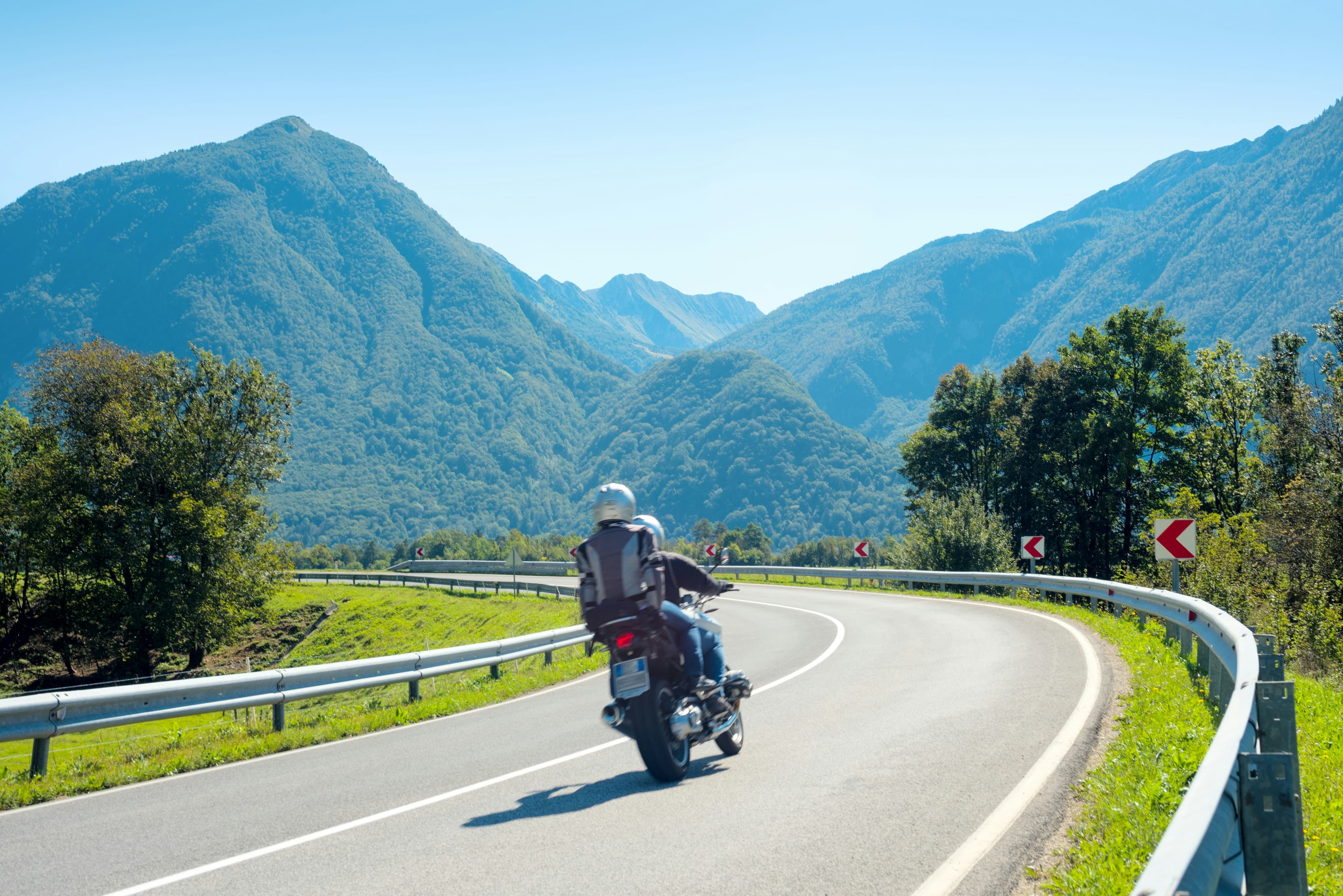A rider on a sweeping mountain road heading towards tall green peaks